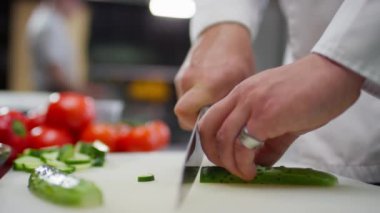 Lokanta mutfağında çalışırken taze salatalığı bıçakla doğrayan tanınmamış bir erkek şefin ellerini yakın plan çek.