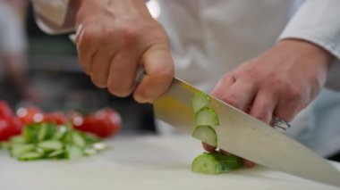 Lokanta mutfağında yemek pişirirken salatalıkları dilimleyip kesen erkek şefin yakın çekimleri.