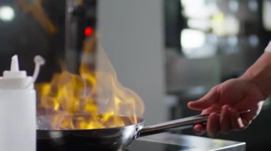 Yavaş çekimde, erkek şefin ateş yakmak için çakmak kullanırken yakın plan çekimleri, sonra da restoran yemekleri pişirirken tavaya sebze atıp alev alması.