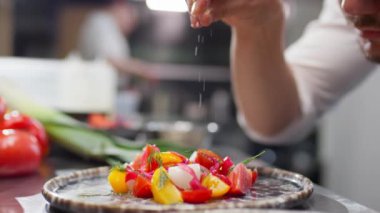 Lokanta mutfağında yemek pişirirken servis edilen taze sebze salatasını tuzlayan erkek şef.