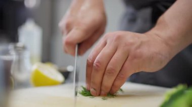Yemek hazırlarken taze dereotu bıçakla kesen erkek aşçının yakın çekimleri.