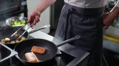Erkek aşçının tavada patates ve balık filetosu kızartırken dil kullanması.
