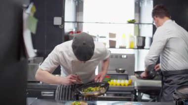 Aşçı yamağı, restoran mutfağında baş aşçıya yardım ederken tabakta balıkla pişirilmiş sebze servis ediyor.