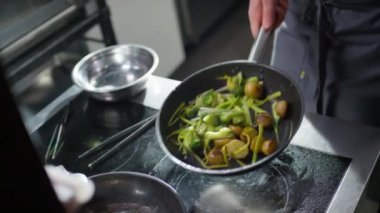 Lokanta mutfağında yemek pişirirken aşçının tavaya pırasa, brokoli ve patates attığı yüksek açı.