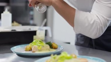 Şef, restoran mutfağında meslektaşının yardımıyla çalışırken tabağa tuz ve baharat ekliyor.