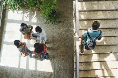 Yüksek açılı bir bakış açısıyla bir grup öğrencinin okul kampüsünde bir arada durup konuşması.