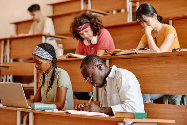 多族裔学生群体坐在大学的课堂上做功课 — 图库照片