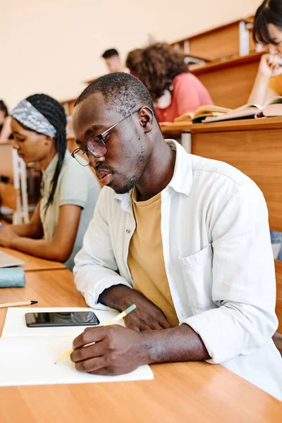 戴眼镜的非洲学生在大学礼堂的课桌前专心致志地准备笔试 — 图库照片