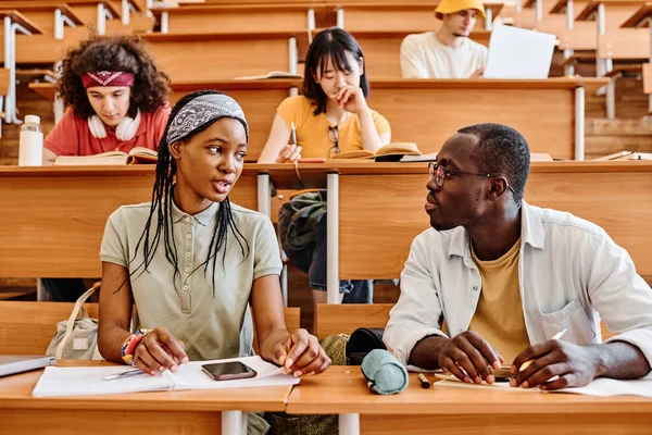 讲座期间 非洲学生坐在礼堂的课桌前互相交谈 — 图库照片