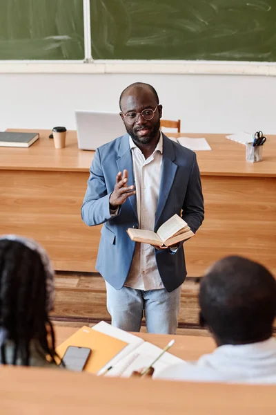 大学の講堂に立っている学生に講義をする本を持つアフリカの教師 — ストック写真