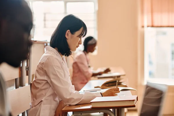在大学讲座期间 亚洲医科学生在课桌边做白衣笔试 — 图库照片