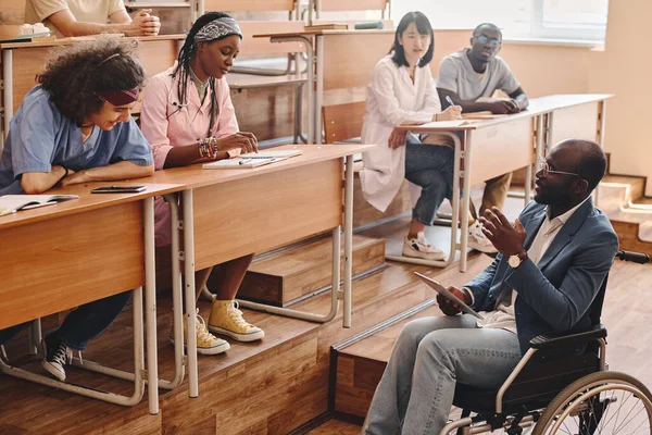 障害のあるアフリカ人教師が車椅子に座り 大学の医学生のために講義を読む — ストック写真