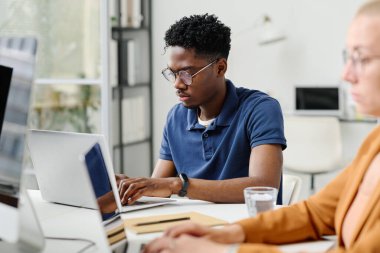 Çevrimiçi işine konsantre olan Afrikalı genç programcı, ofisteki meslektaşlarıyla masada otururken dizüstü bilgisayarında daktilo yazıyor.