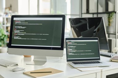 Bilgisayarın yatay görüntüsü ve ekranda yeni bir yazılım var. Kodlar ofisteki programcının masasında duruyor.
