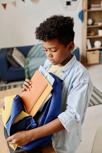 アフリカの少年は 部屋に立って学校の準備をするために本をパックするために彼のスクールバッグを開く — ストック写真