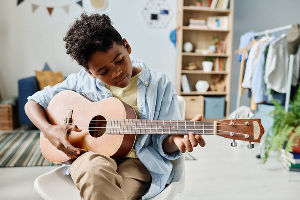 African boy sitting on chair and concentrating on his play in guitar, he remembering the notes during home lesson