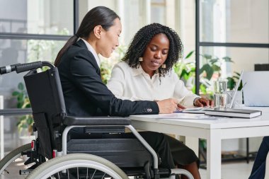 Tekerlekli sandalyedeki Asyalı iş kadını ofisteki meslektaşıyla iş sözleşmesini tartışıyor.
