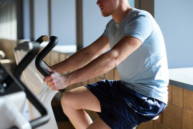 Spor salonunda bisiklet egzersiz ekipmanları üzerine çalışan genç kaslı adamın yakın çekimi.