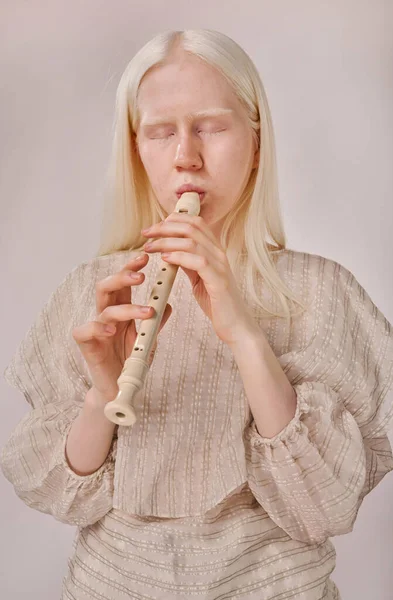 Portrait of albino girl enjoying playing on musical instrument standing on white background