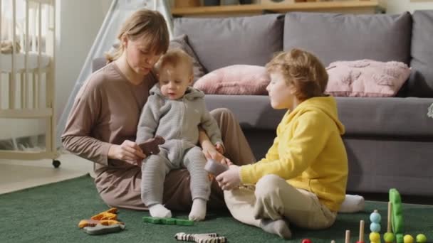 愛する母保持おもちゃと何かを伝える赤ちゃん男の子に座って彼女の膝の上に少し息子と遊んでいる間に床の上にリビングルーム — ストック動画