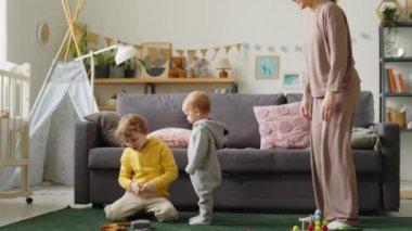 Küçük çocuk ilk adımlarını atıyor ve evdeki çocuk odasında anne ve kardeşiyle oynuyor.