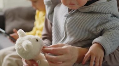 Annenin bebekle oturduğu ve elinde oyuncak tutarken büyük oğlunun tabletle oynadığı sahneyi çek.