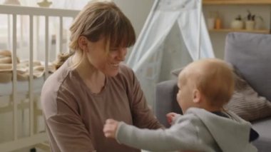 Neşeli bir anne çocuğunu kaldırıyor ve mutlu bir şekilde gülümsüyor evde ilk adımlarını atıyor.