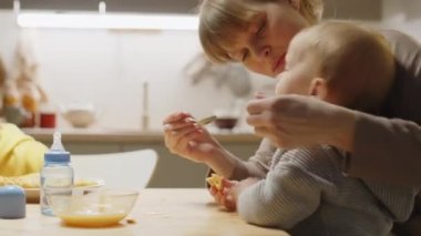 Annesi mutfak masasında bebeğini beslerken büyük oğlu onların yanında yemek yiyor.