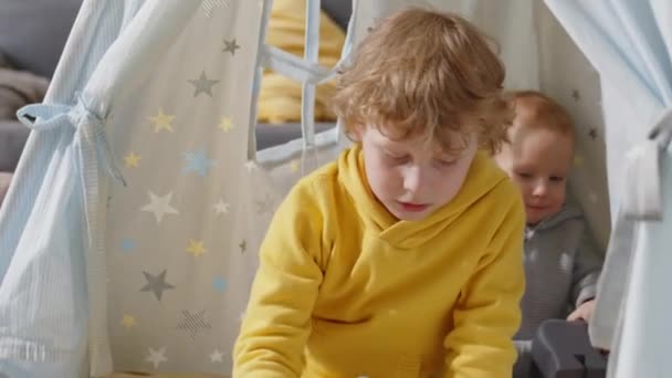 小さい男の子遊びますおもちゃとともにティーピーに座っている間に赤ちゃん兄で子供部屋 — ストック動画