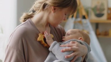 Sevgi dolu anne kucağında oğlunu sallıyor. Evde çocuk odasında uyuyor.