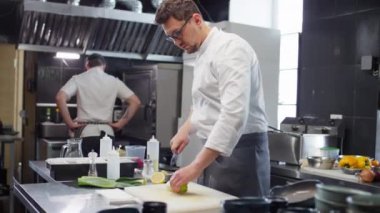 Üniformalı erkek aşçı restoran mutfağında yemek pişirirken taze pırasa kesiyor.