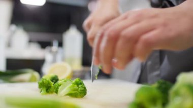 Lokanta mutfağında yemek pişirirken brokoli kesen erkek şefin yakın çekimleri.
