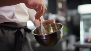 Restaurant mutfağında duran ve kasede malzemeleri çırpan önlüklü, tanınmayan bir aşçı.