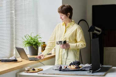 Genç bayan fotoğrafçı fotoğraf stüdyosunda fotoğraf çekerken dizüstü bilgisayarla çalışıyor.
