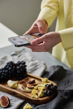 Genç bir kadının akıllı telefonuyla ahşap tepside taze meyve fotoğraflarını çekerken.