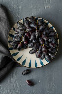 Gri arka planda plaka üzerinde olgun siyah üzümlerin yüksek açılı görüntüsü