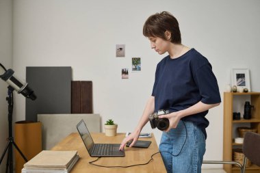 Kamerayı laptopa bağlayan genç fotoğrafçı stüdyoda çalışırken fotoğraflarını izliyor.