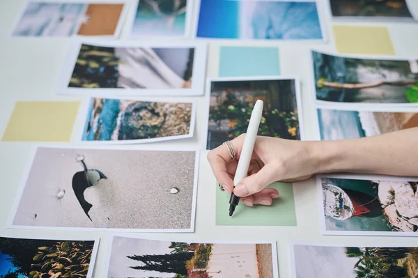 Close-up of photographer making notes on sticky note among professional photos