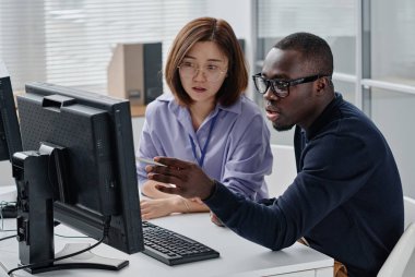 Afrikalı Amerikalı programcı meslektaşıyla ekranı gösterip sunumu tartışıyor.