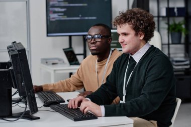Ofisteki takım çalışması sırasında bilgisayardaki yeni yazılımlar için bilgisayar kodlarıyla birlikte çalışan iki bilişim uzmanı.