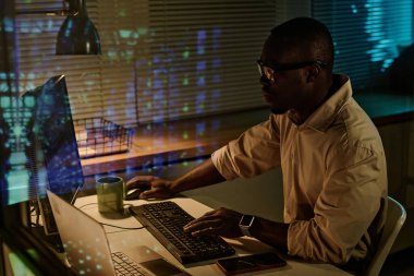 Ofiste fazla mesai yaparken bilgisayarda klavye güvenlik kodlarını yazan Afrikalı Amerikalı iş adamı