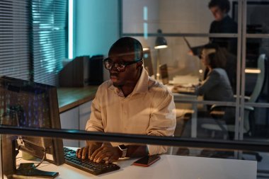 Klavyede yazan ve gece geç saatlere kadar bilgisayarla çalışan Afrikalı Amerikalı geliştirici ve arka plandaki meslektaşları