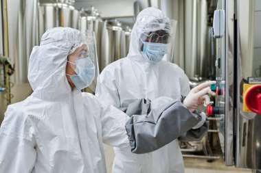 Kimya fabrikasındaki işleri sırasında ekipmanları birlikte kontrol eden koruyucu kostümlü birkaç işçi.