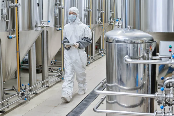 stock image Worker in protective wear using digital tablet while walking along the workshop at chemical factory