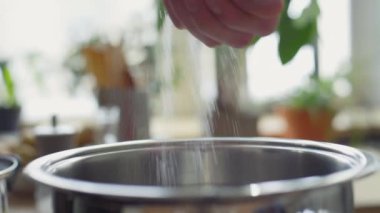 Erkek eli, yemek pişirirken çelik kaba tuz dökerken yakın çekim.