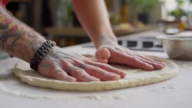 Un kaplı mutfak masasına pizza hamuru seren erkek aşçıyı yakından çek.