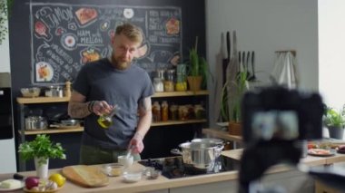 Yemek blogcusu havan topuna zeytinyağı ekliyor ve mutfakta yemek pişirirken tokmak kullanıyor ve profesyonel kamerayla video dersi kaydediyor.