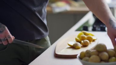 Erkek aşçının mutfakta yemek pişirirken taze patatesleri bıçakla yarıya kestiği sahneler.