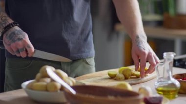 Mutfakta yemek pişirirken taze patatesleri bıçakla kesen tanınmayan bir adamın görüntüsü.