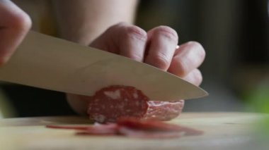 Erkek eli yakın çekimde bıçakla salamı ince dilimlere ayırıyor.